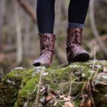 Frau in Wanderschuhen steht auf einem mit Moos bewachsenen Felsen