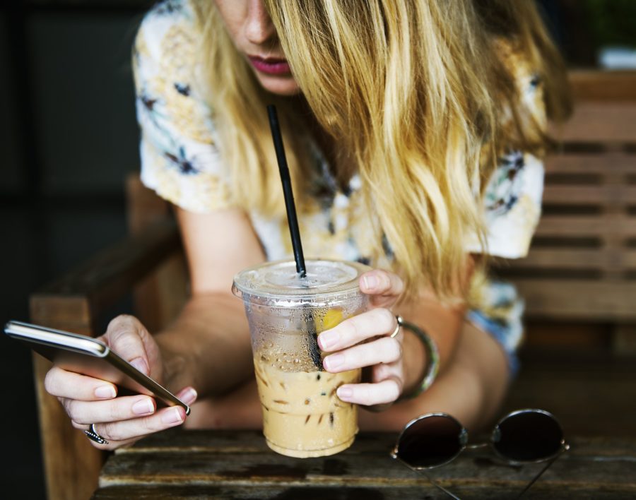 Frau sucht etwas am Handy und trinkt Kaffee